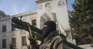 Боец от сирийската опозиция пред сградата на регионалното правителство в град Хама пред фасада с портрет на сваления президента Баша Асад